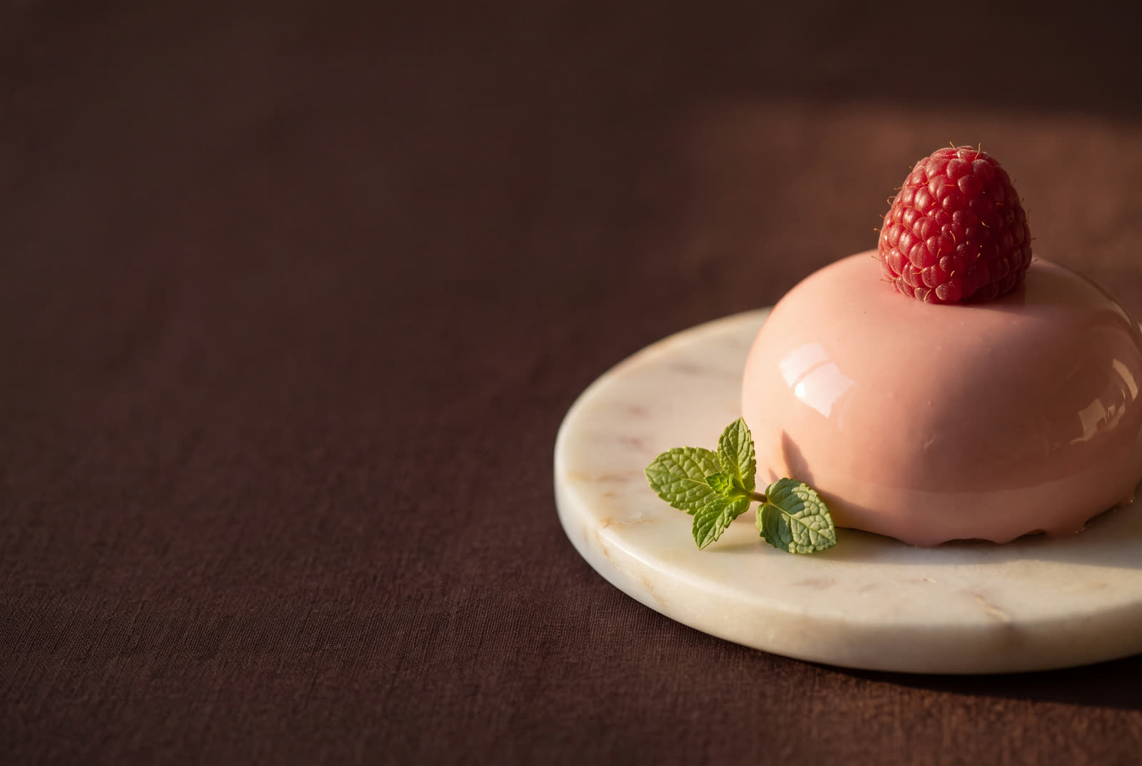 A pink petit gâteau with a raspberry on a marble plate